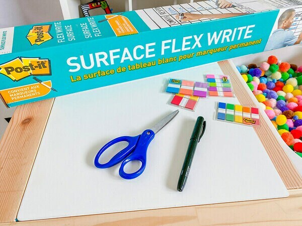 Un emballage de la Surface Flex Write Post-it® à côté de ciseaux, Languettes adhésives et Onglets Post-it® et des pompons.