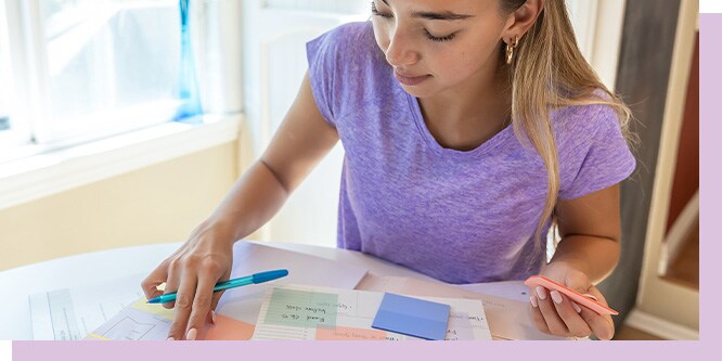 Teen student using colorful Post-it notes in green, orange, and pink to organize schoolwork at a bright desk in a back-to-school setting.
