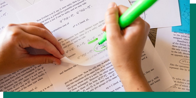 Hands holding a sheet and highlighting text on printed documents with a green marker.
